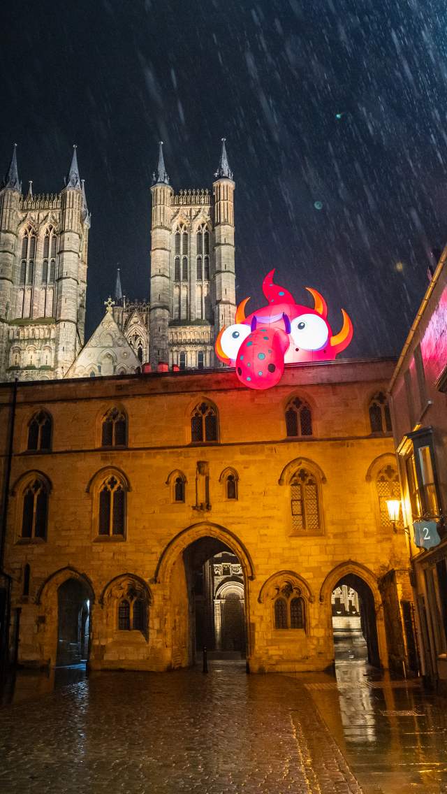 A rainy nighttime shot of Lincoln Cathedral with an inflatable monster on top of a building in the foreground