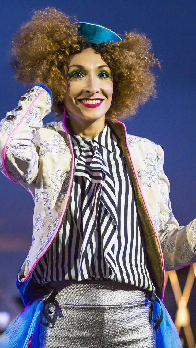 Performer in bright clothing from Transe Express theatre company in front of the Cristal Palace Chandelier