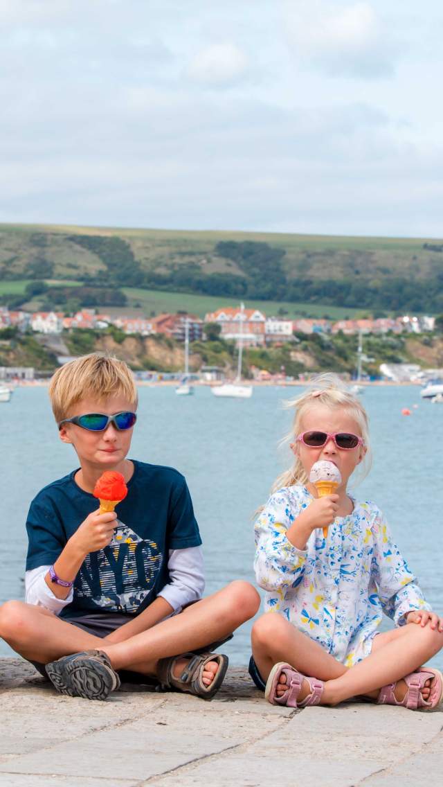 Three children eating ice cream in front of Swanage Bay Dorset