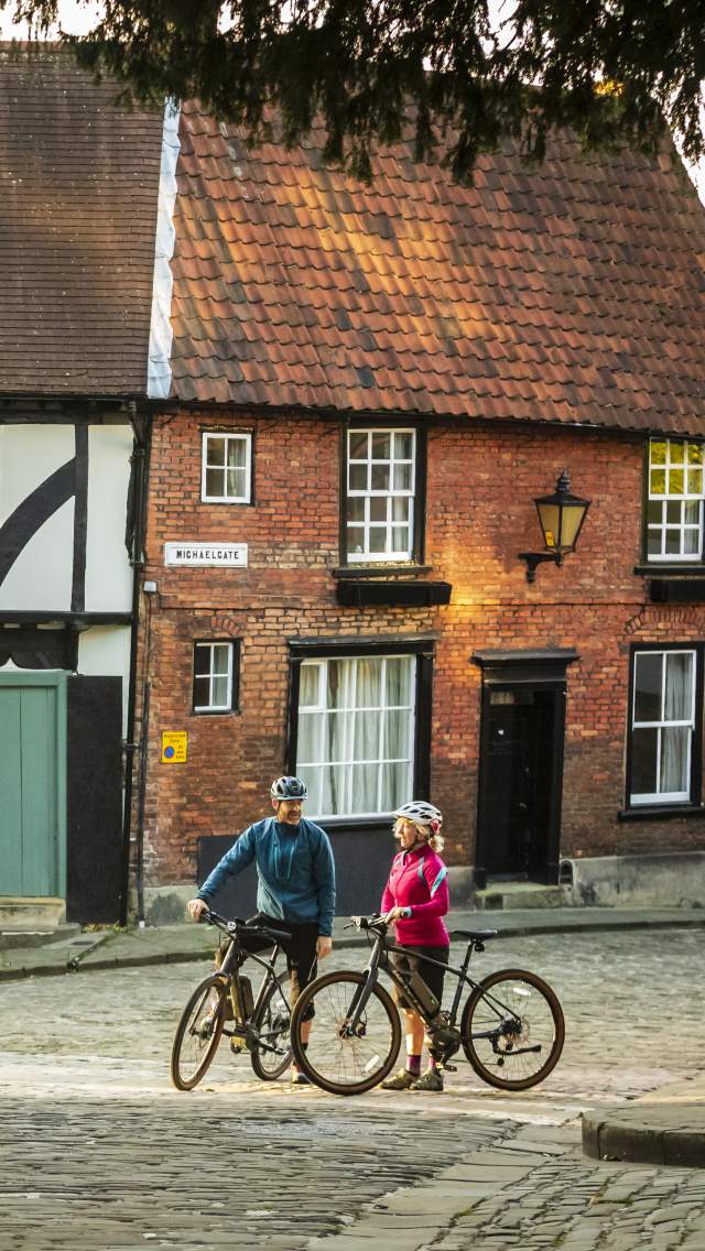 A couple of cyclists stood with bikes on the cobbled streets of Lincoln Steep Hill.