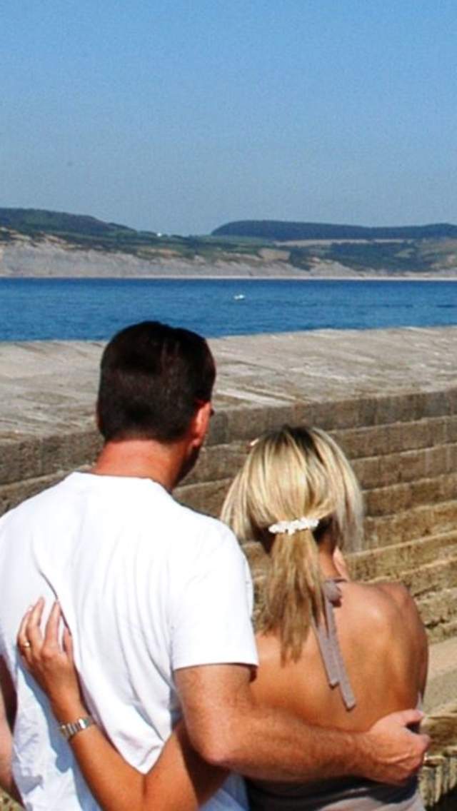 A couple looking towards The Cobb at Lyme Regis with stunning views along Dorset's coast