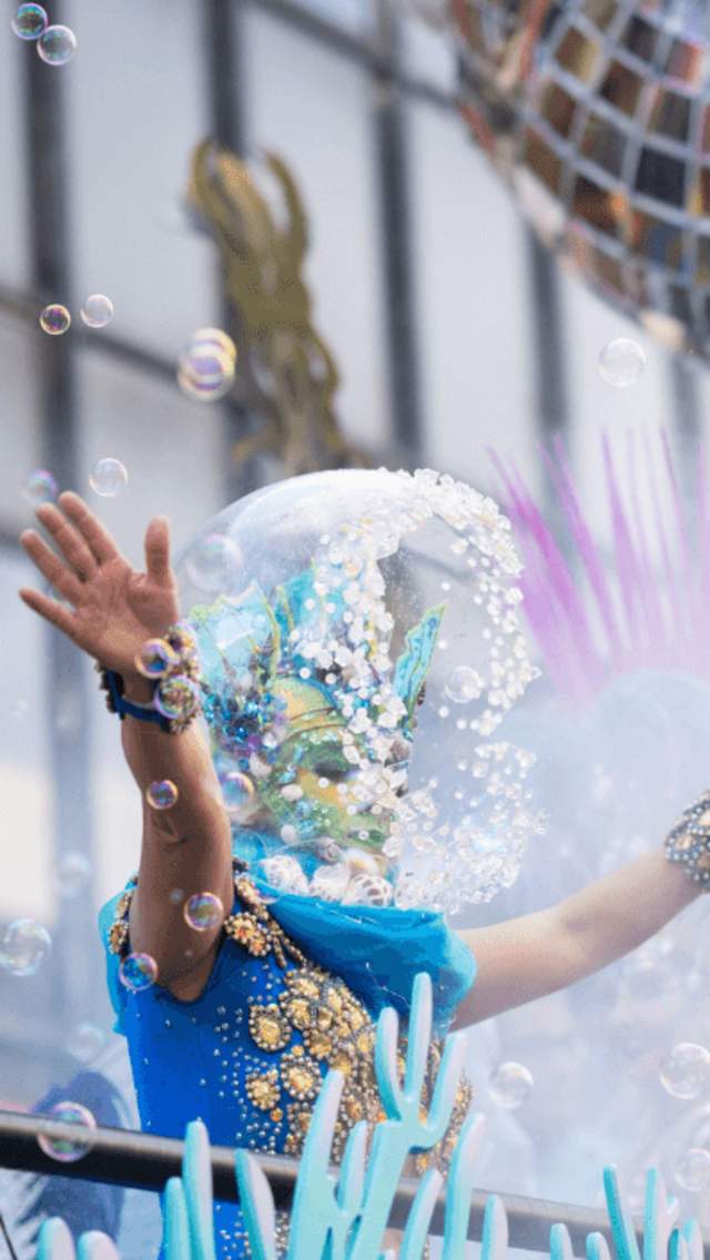 Woman dressed as a sea creature with a bubble on her head standing on a float surrounded by bubbles and a disco ball