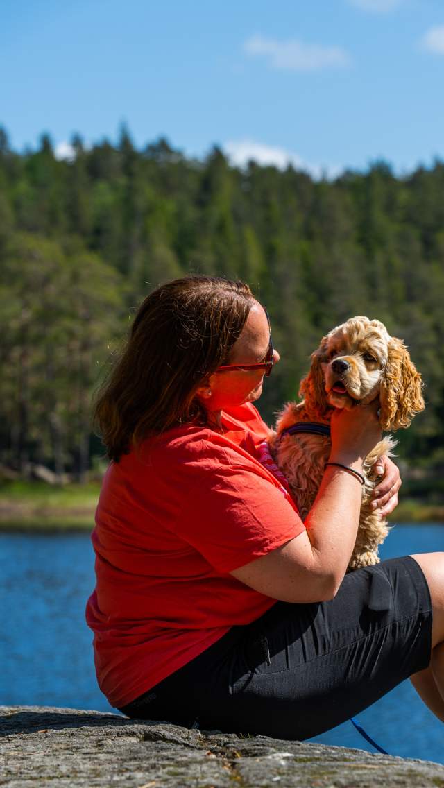 Lady sitting with her dog on her lap by a pond