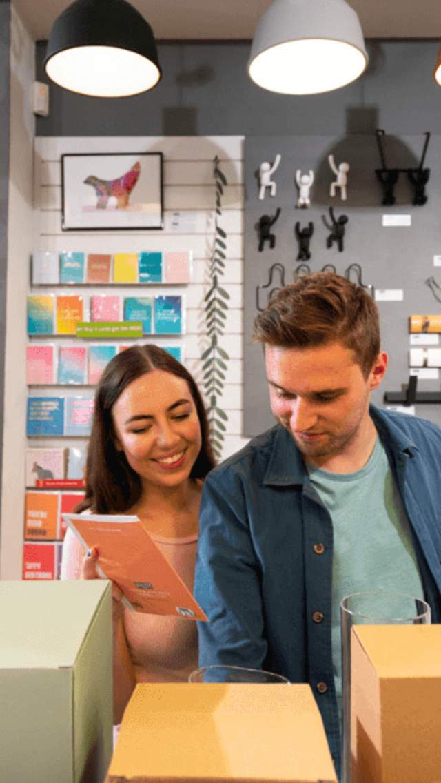 A young woman and male in their mid twenties are browsing amongst colourful homeware pieces and 'nick naks' in a quirky store.