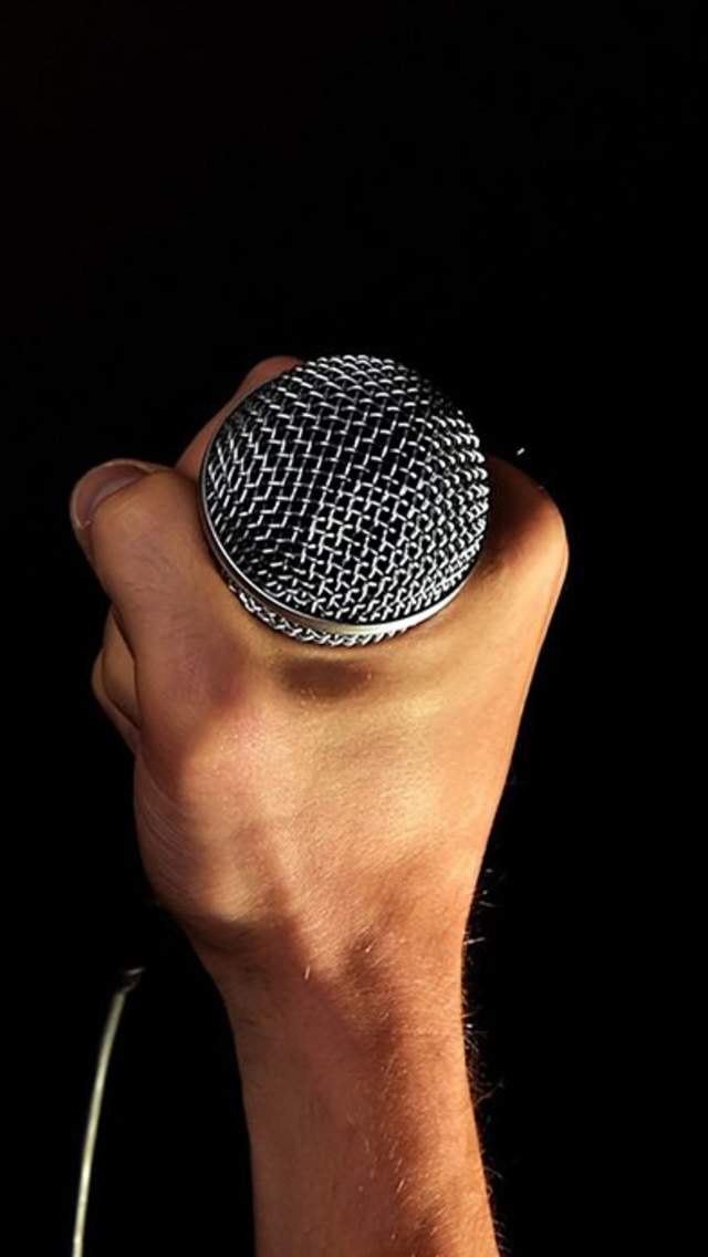 A hand holding a stand up microphone with a black background.
