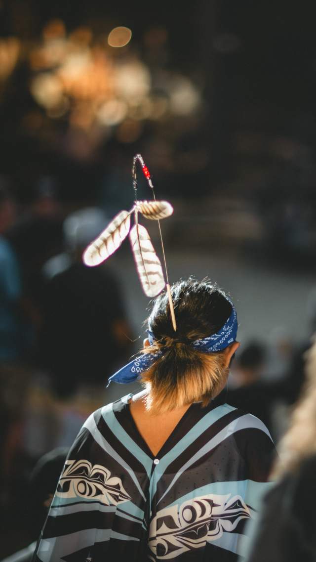 Young women with traditional Snuneymuxw regalia, picture taken from behind, woman walking away