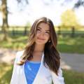 Headshot of a woman with long brown hair, blue shirt and white blazer