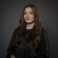 Caucasian lady in a black top poses for a headshot in front of a dark gray backdrop