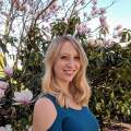 Headshot of Alayna Newman in a blue shirt without shoulders standing by a magnolia tree in bloom.