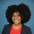 woman with black hair poses in a red shirt and blue blazer