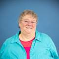 woman poses in a blue jacket and pink shirt wearing glasses