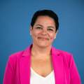 woman with black hair poses in a pink blazer and white blouse