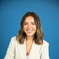 woman with brown hair poses in a cream colored blazer