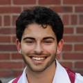 Headshot of Eli Panero in a white shirt with red sash in front of a brick wall.