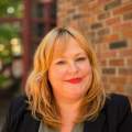A headshot of Fiona in a dark blazer in front of a brick wall.