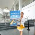 A photo of Robin Cortese holding a "Welcome to Syracuse" sign