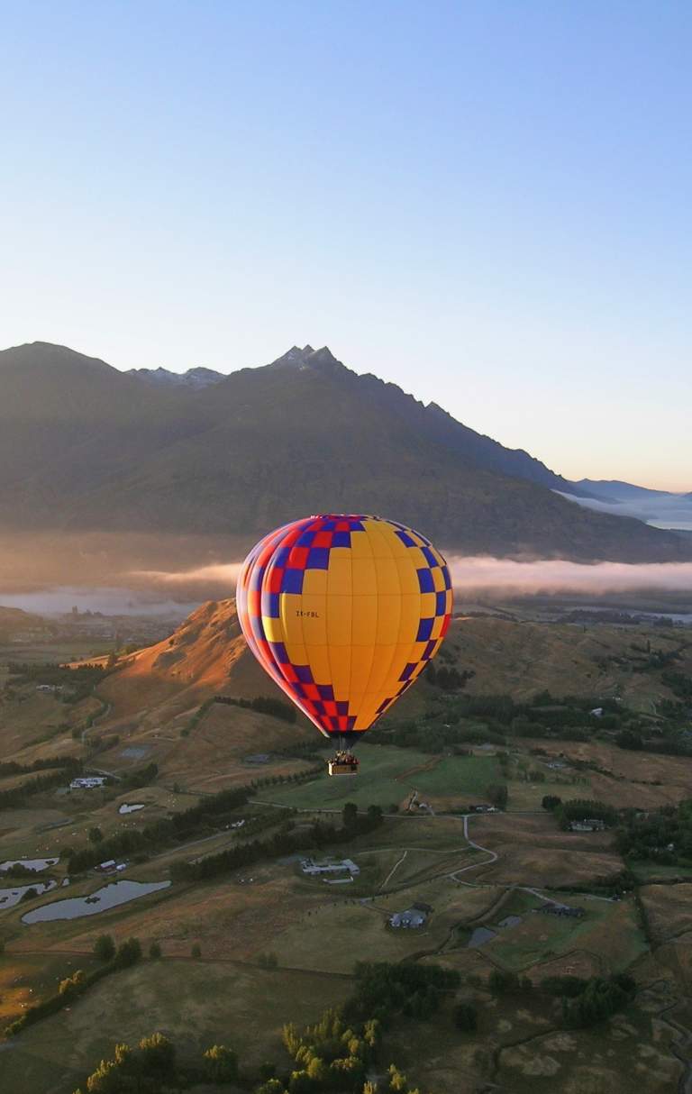 Shot of a hot air balloon at sunrise overlooking a green valley and mountain