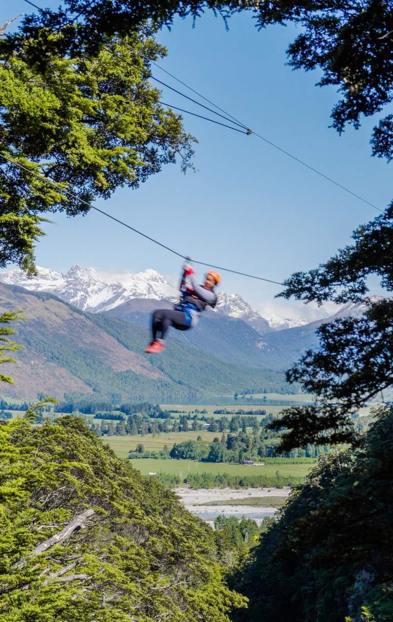 Person ziplining with snow-covered mountain in the back