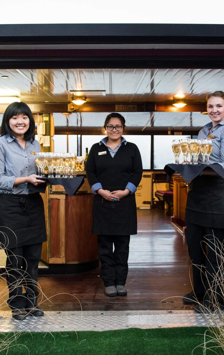 Waitresses waiting to greet guests onto a boat with trays of champagne