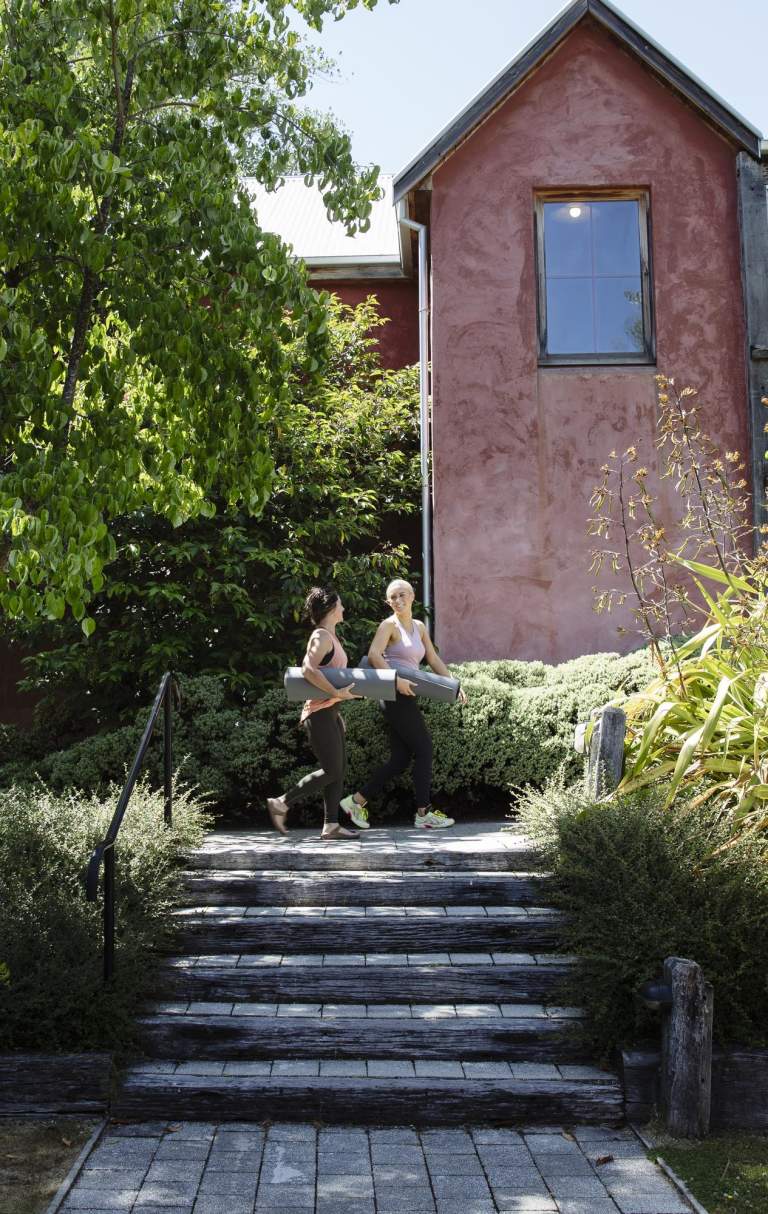 Two women walking outside a health centre holding yoga mats.