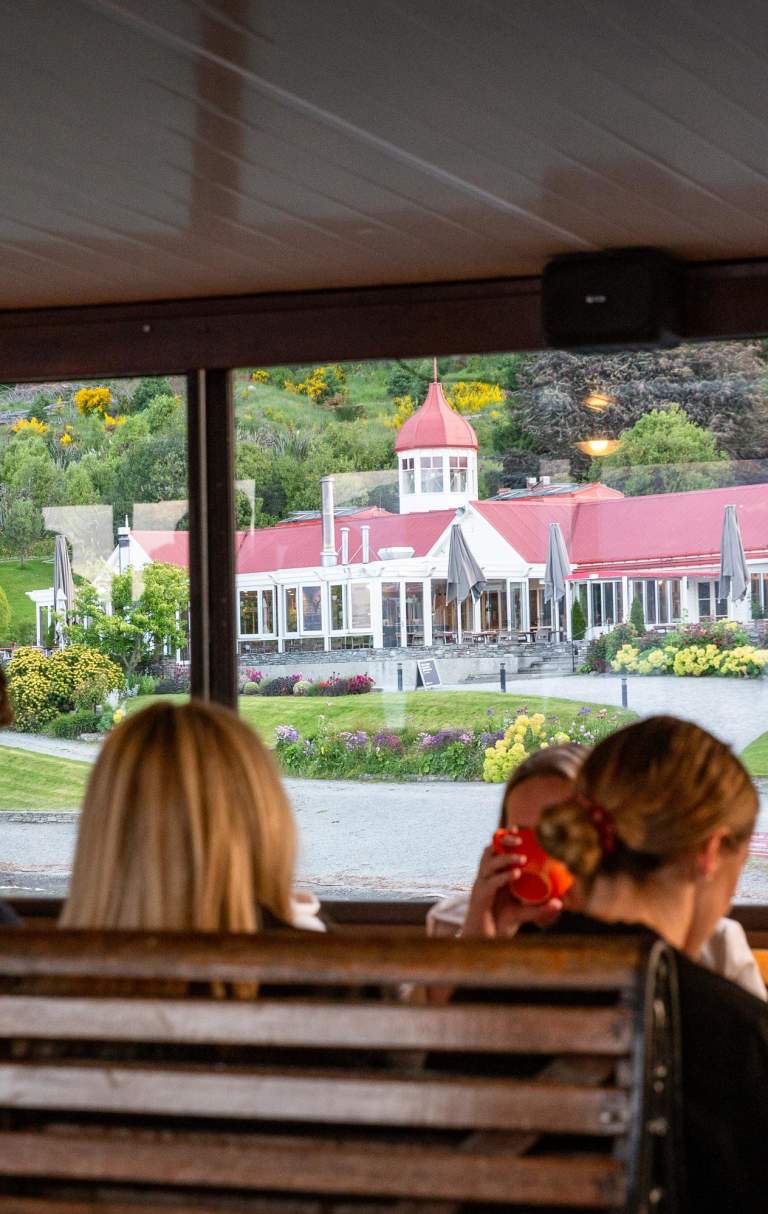 A group of people sitting on the TSS Earnslaw with a view of Walter Peak through the windows