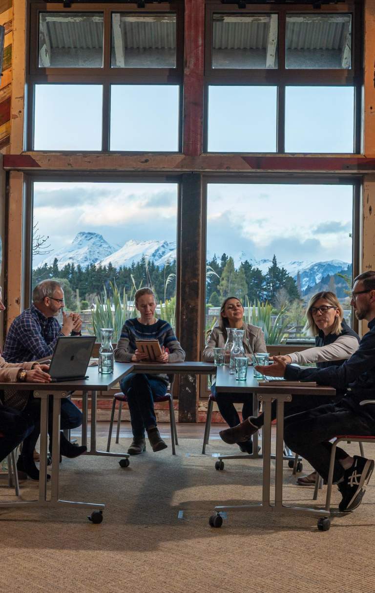 A small group of people sitting around a conference table with view of mountains and trees from the window