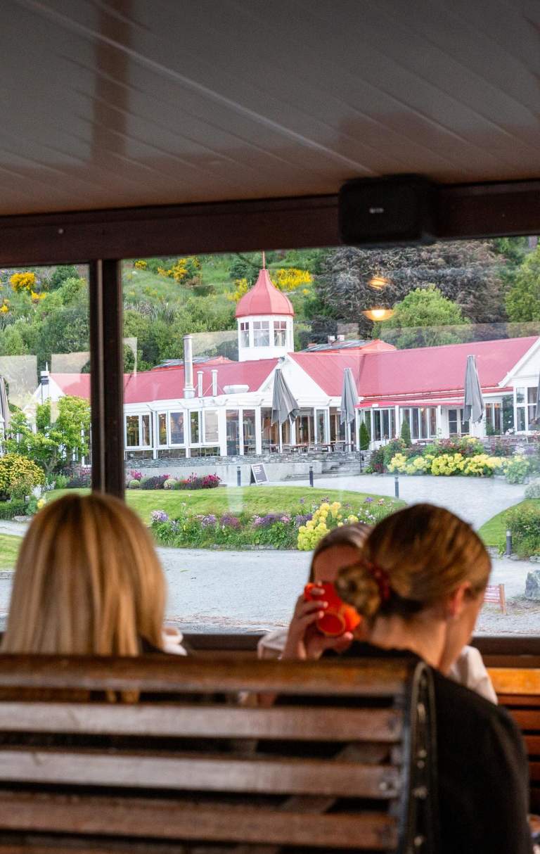 A group of people sitting on the TSS Earnslaw with a view of Walter Peak through the windows