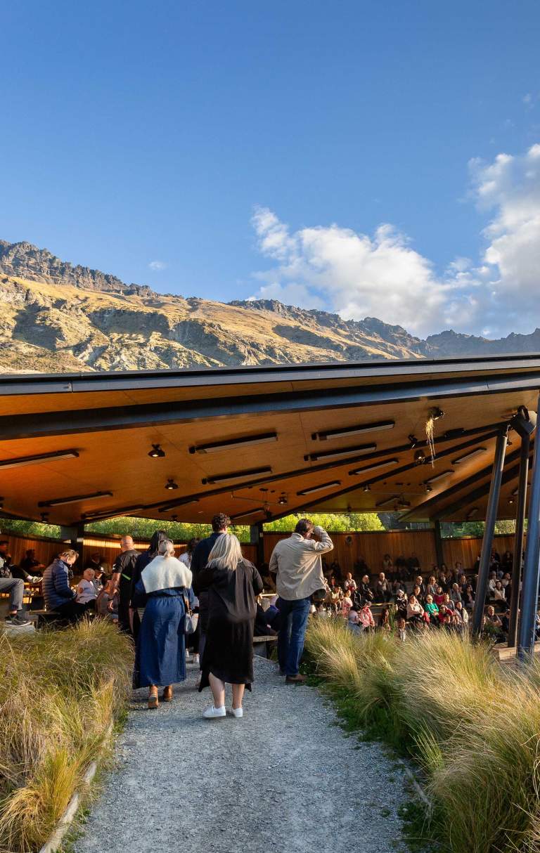 A group of people gather at an outdoor venue surrounded by mountains and trees