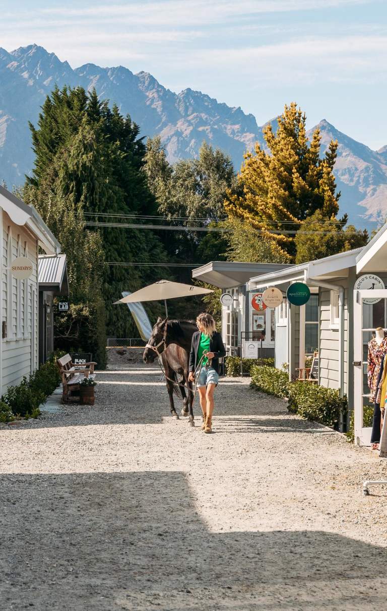 A lady walking a horse on a path lined with boutique cabins and shops