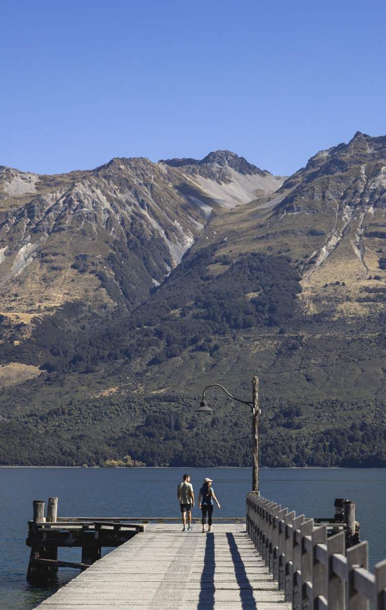 Two people standing on Glenorchy Wharf with mountains in the background