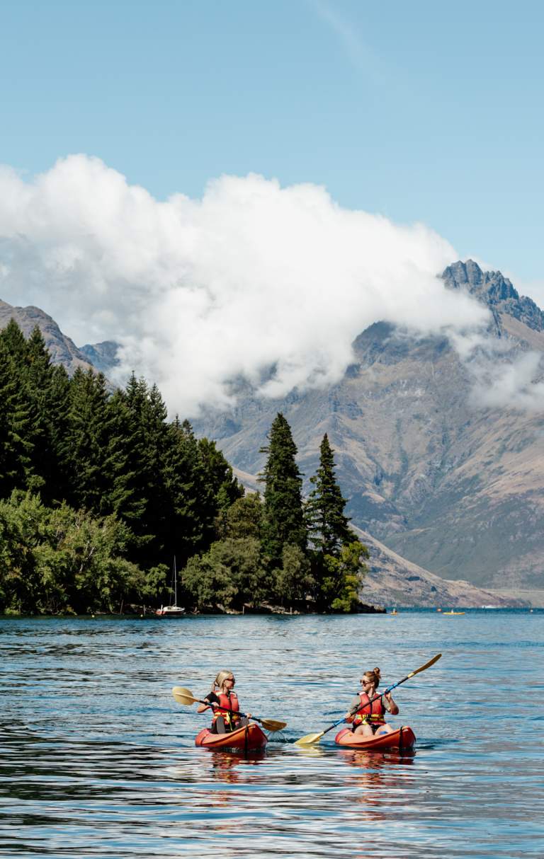 Two people kayaking in Queenstown Bay with mountains in the background