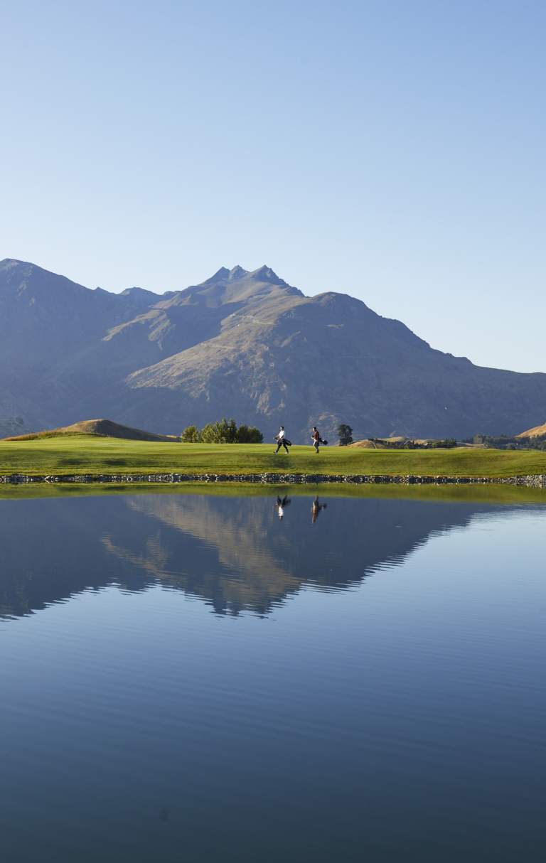 Wide shot of a golf course with lake reflecting mountains