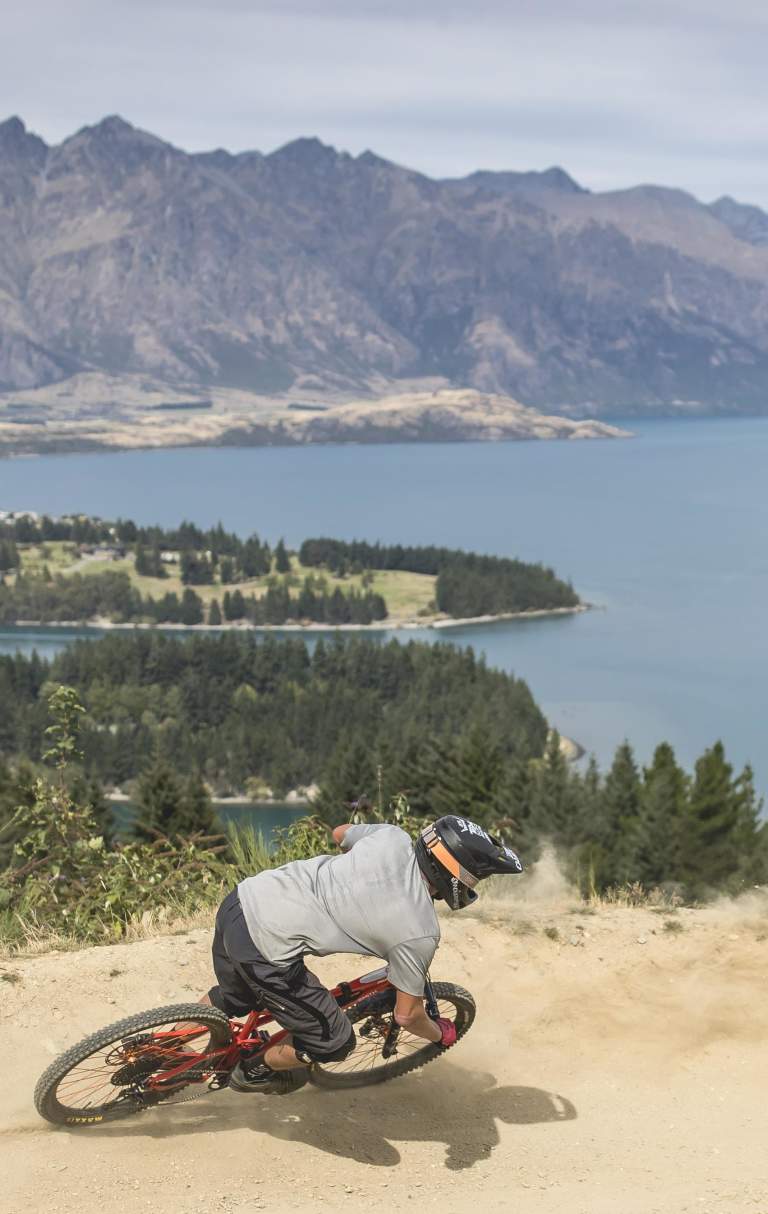 Person biking Queenstown Bike Park with view overlooking lake Whakatipu and the Remarkables mountain ranges