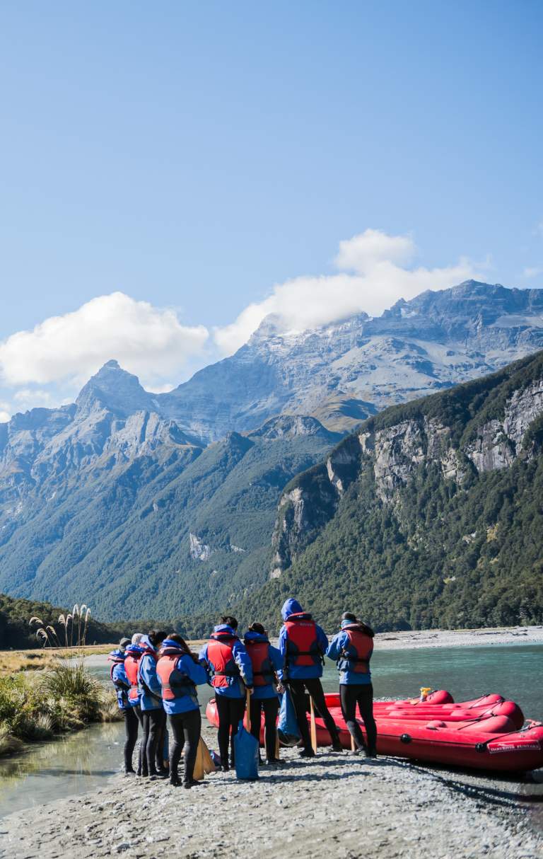 A group of people with inflatable kayaks standing by a river and surrounded by mountains