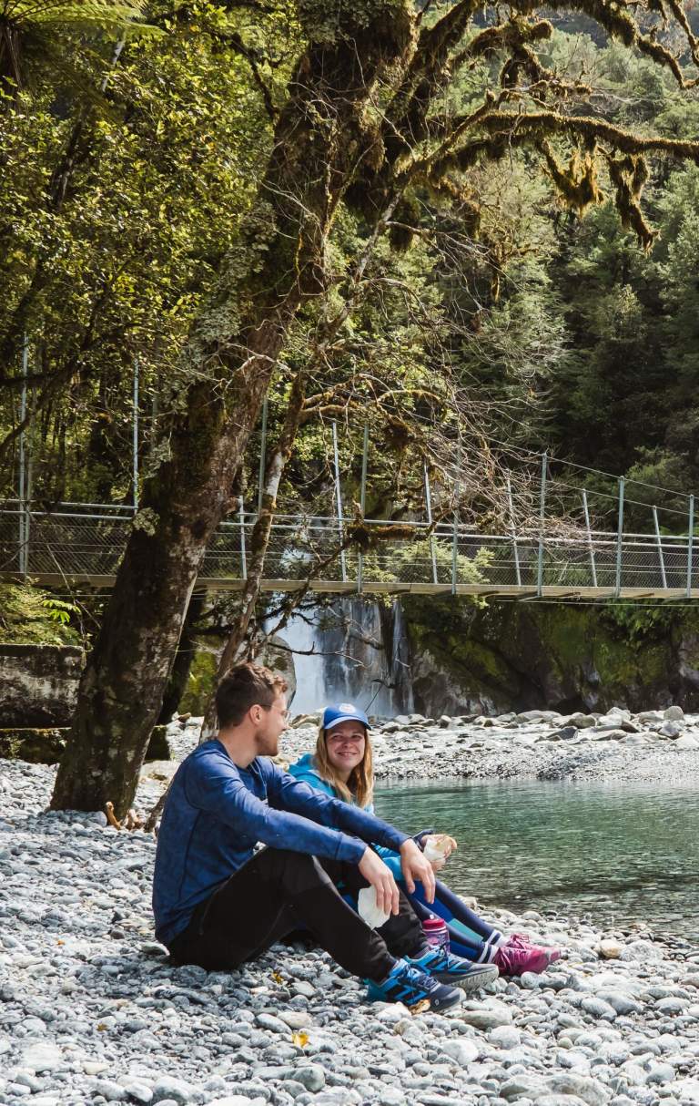 Two people sitting next of a river surrounded by bush