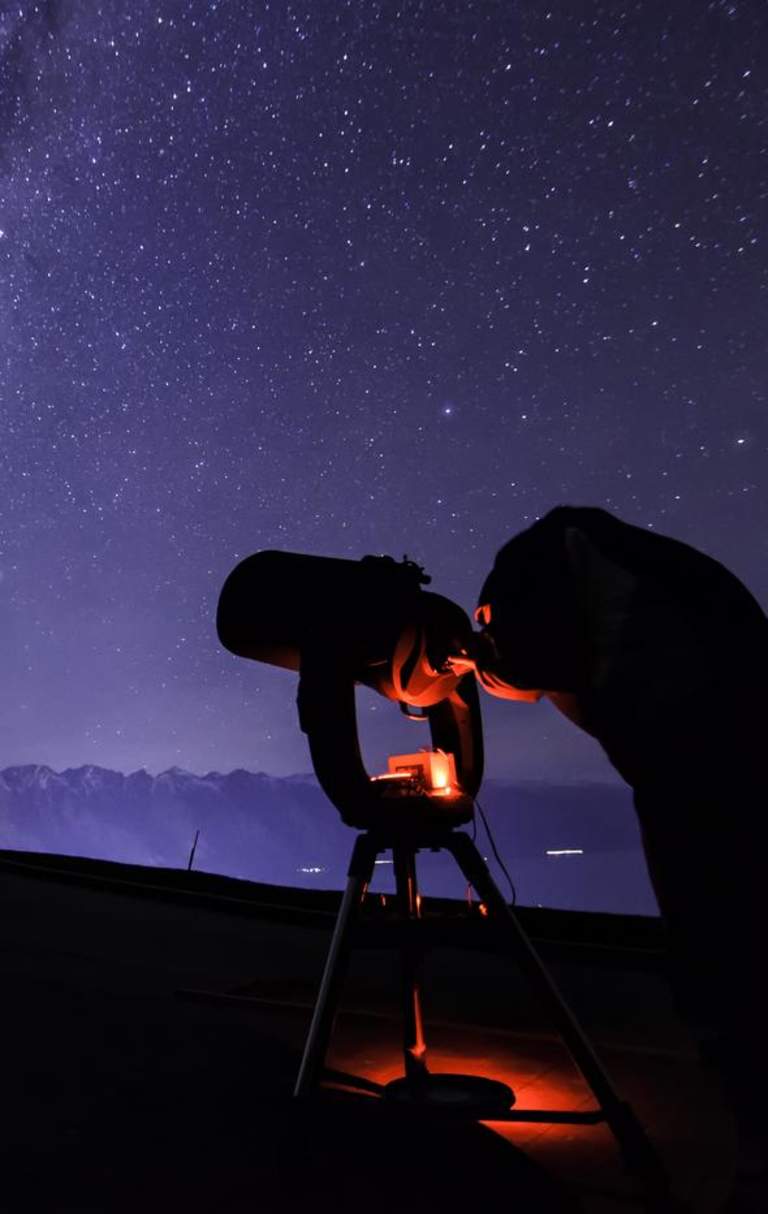Person with telescope stargazing underneath the milky way near The Remarkables mountain range