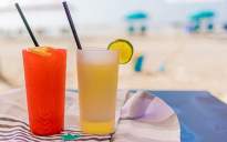 Two cocktails sitting on the beach, one is red one is yellow. Thye are sitting on a towel.