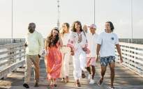 A group of seven walk down the pier, smiling and wearing outfits from Port Aransas boutiques