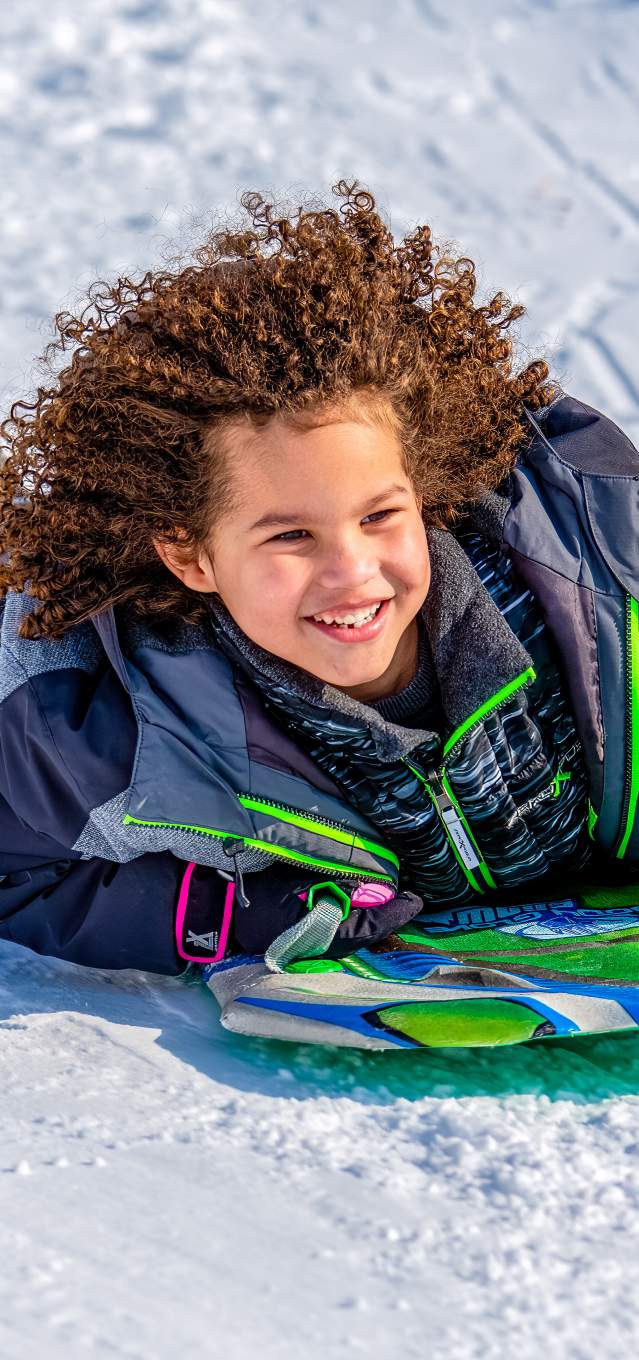 A young child sleds down a snowy hill on a green sled
