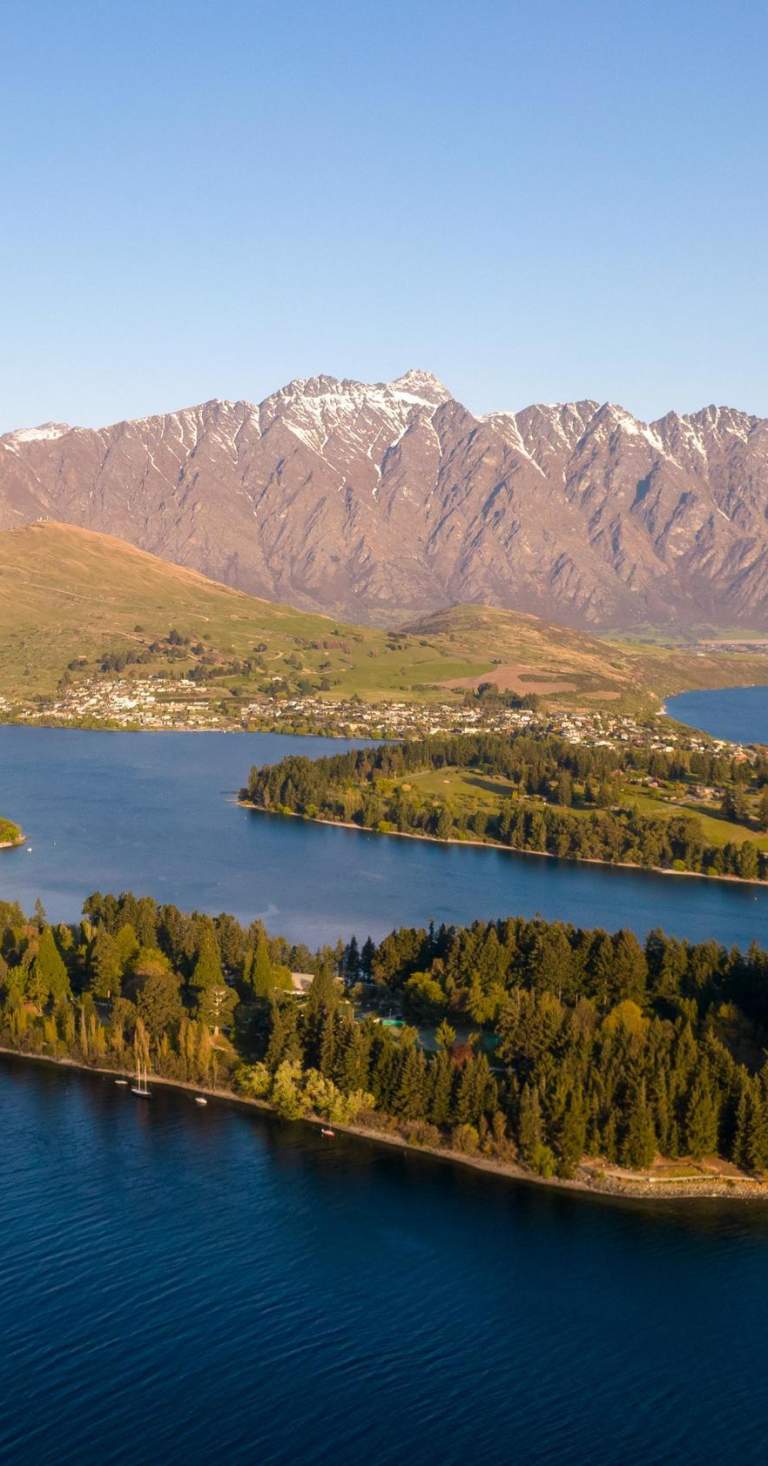 A panoramic view from Bob’s Peak overlooking Queenstown, Lake Whakatipu, the forested peninsula of Queenstown Gardens, and the Remarkables mountain range in the distance.