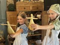 girls in 1800s dresses with corn husk dolls