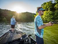Two men hold fishing poles off a boat in the middle of the river