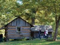 people walking by a historic log cabin