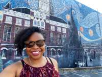 lady smiling in front of a large mural