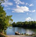 Summer view of Shenandoah River in Page Valley, Virginia, with calm water, shoreline trees, blue sky, and a small dock on the river banks.