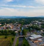 Aerial view of Luray surrounded by lush greenery and mountains, showcasing streets, buildings, and a river.
