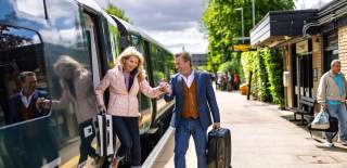 A couple disembark a train carrying suitcases at Kingham station