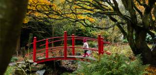 Child in bobble hat and pink coat crossing a bridge at Batsford Arboretum