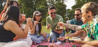 Group of friends enjoying sushi and bubble tea on a picnic blanket in the park