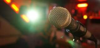 Photograph showing a microphone in a stand - the lighting behind suggests it's in a club